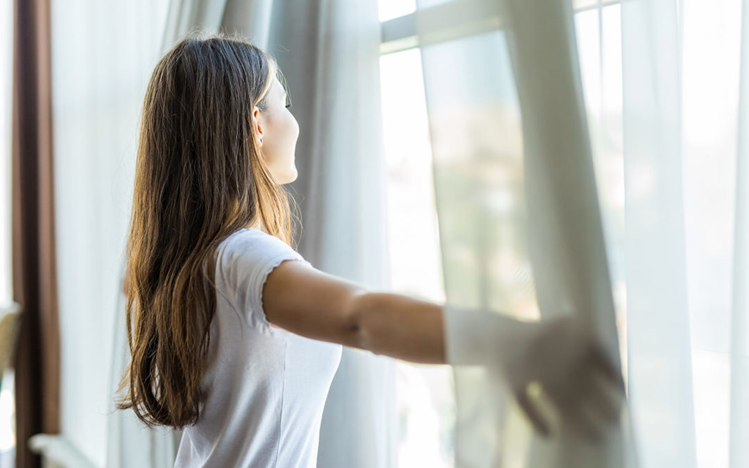 Young pretty girl opening curtains in a bedroom