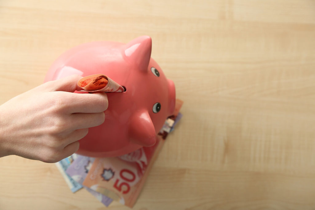 inserting Canadian dollars into pink piggy bank